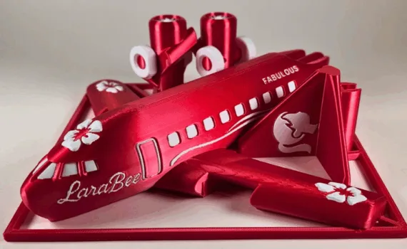 A dramatic red multicolor 3D-printed airplane kit card with floral accents and the name “LaraBee,” printed as part of a christmas drive 3D printing community project.