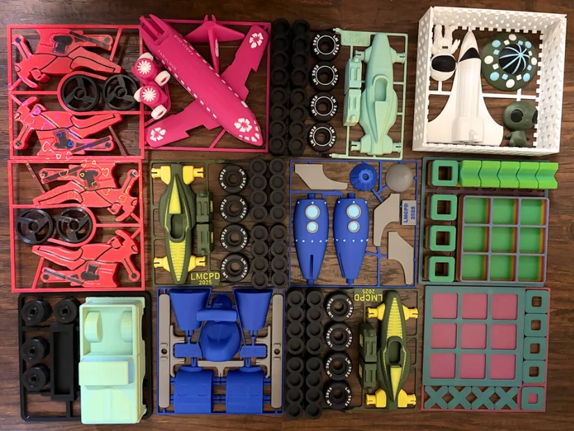 A collection of 3D-printed multicolor toy kits including race cars, planes, rockets, and puzzle trays, displayed neatly in frames