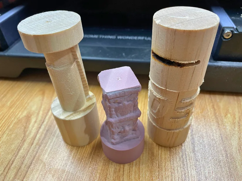 Three test pieces from Snapmaker 4-axis CNC module showing failed attempts at carving, including rough shapes and incomplete 3DWithUs logo engraving