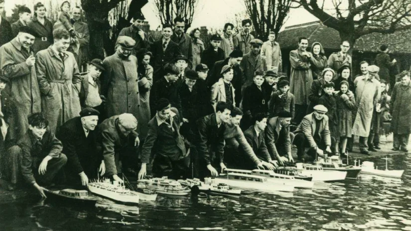 Historic photo of Southend Model Boat Club members launching scale model boats in a pond, surrounded by a large crowd.