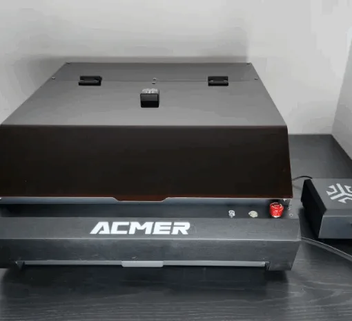 Acmer P3 24W enclosed laser engraver with protective lid and external control module on a black desk