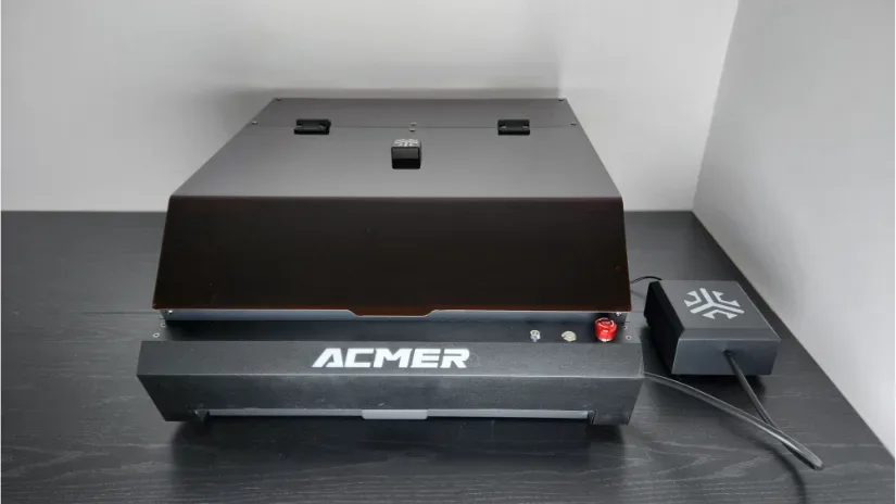 Acmer P3 24W enclosed laser engraver with protective lid and external control module on a black desk