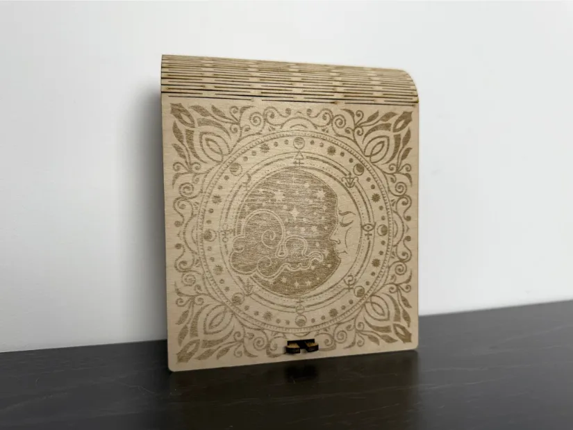 A wooden box featuring an intricately laser-engraved moon within a circular pattern accented by stars, paired with a flexible living hinge for smooth opening. Title for Metadata and Gallery: Moon Engraved Wooden Box with Living Hinge Caption Suggestion: Intricately engraved wooden box with a moon design and a smooth living hinge.