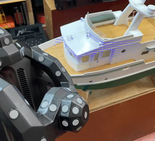 Revopoint Trackit 3D scanner in use, scanning a detailed model boat with visible laser lines projected onto the surface