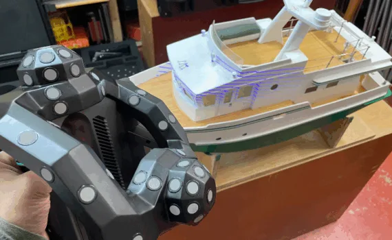 Revopoint Trackit 3D scanner in use, scanning a detailed model boat with visible laser lines projected onto the surface