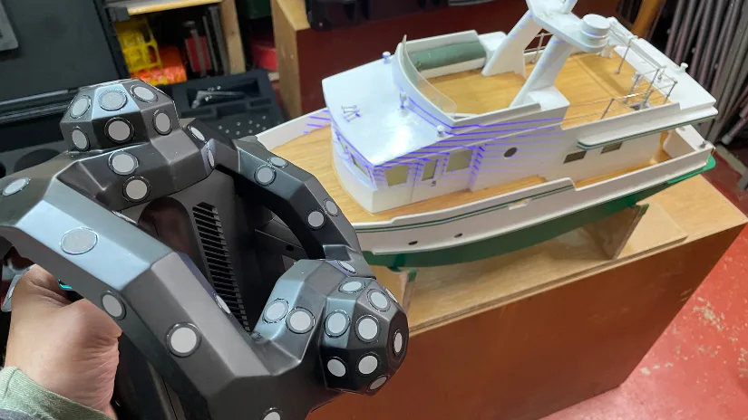 Revopoint Trackit 3D scanner in use, scanning a detailed model boat with visible laser lines projected onto the surface