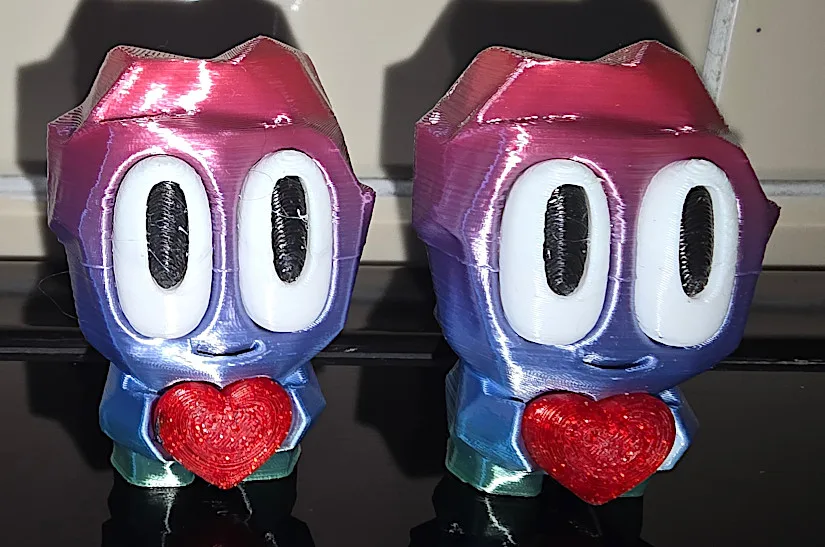 Two multi-color 3D printed Rock People characters by Blob Lab, holding red hearts, printed with dried filament using the EIBOS Series X Tetras system.