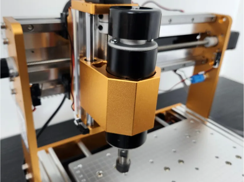 Close‑up of the Lunyee 3018 Pro Ultra’s 500 W spindle mounted on its gold‑anodized aluminum Z‑axis carriage, with linear guide rails and the T‑slot work bed in the background.