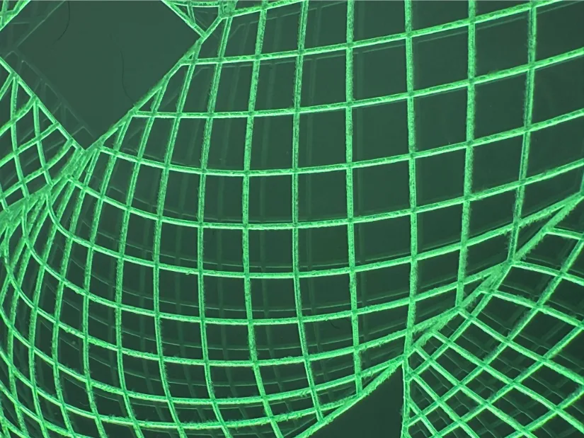 Macro close‑up of the torus‑knot lamp: fine grid grooves engraved into clear acrylic with a 30‑degree V‑bit glow bright green under edge lighting.