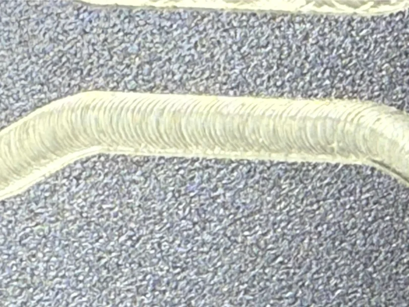 Macro close‑up of machining marks along a milled groove in anodized aluminum, showing uniform scallop patterns left by a 1/8‑inch tungsten‑carbide end mill on the Lunyee 3018 Pro Ultra CNC router.