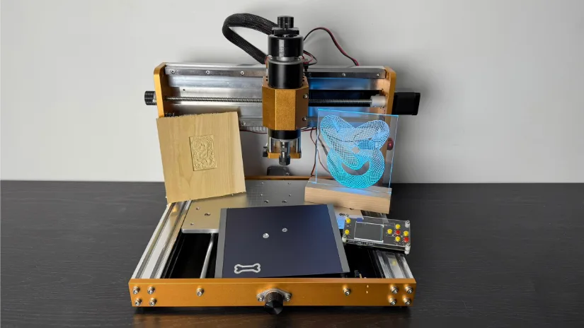 Lunyee 3018 Pro Ultra CNC router displaying three finished test pieces: a relief‑carved basswood plaque, a blue edge‑lit acrylic sign, and a milled black anodized aluminum plate with dog‑bone logo.