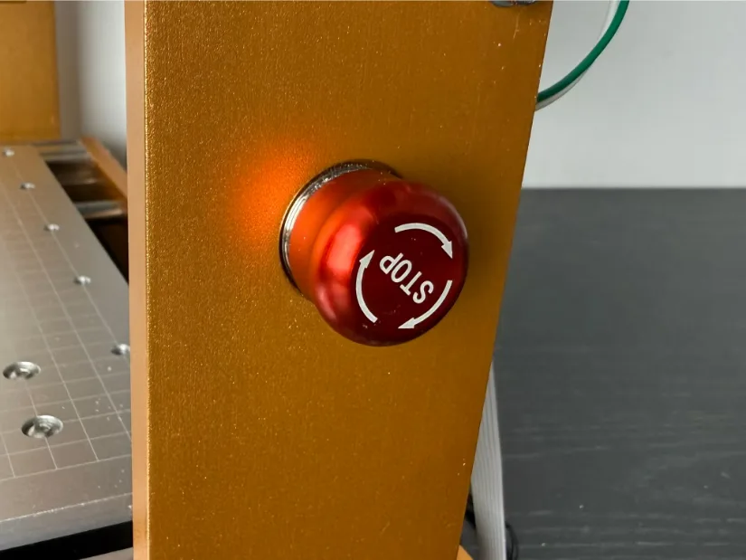 Close‑up of the red emergency‑stop button mounted on the gold‑anodized frame of the Lunyee 3018 Pro Ultra CNC router.