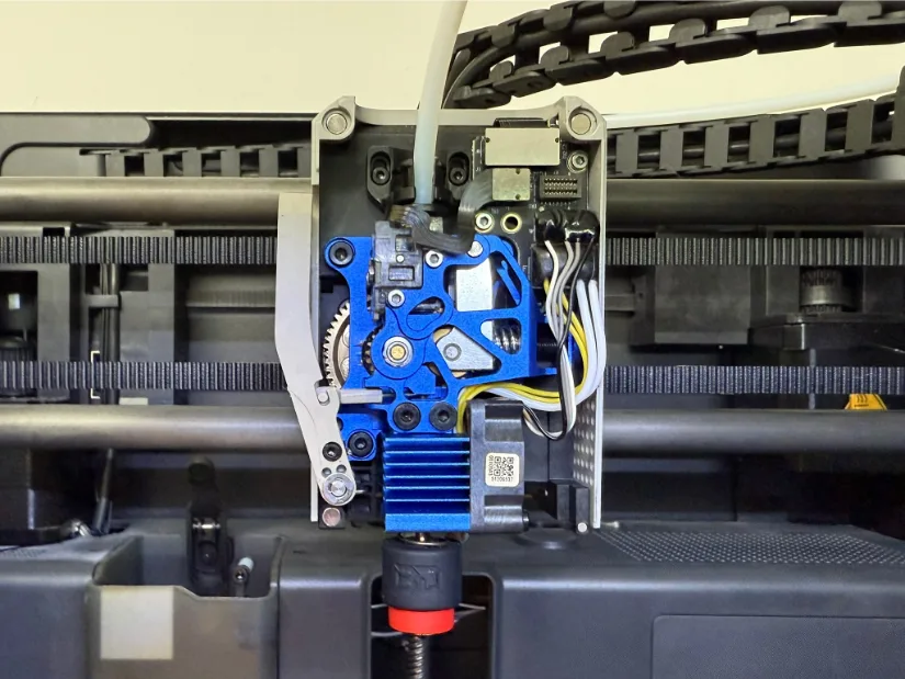 Close-up of a BIGTREETECH Panda Claw CNC-machined aluminum tool-head frame mounted on a Bambu Lab printer, holding the blue Chain direct-drive extruder and an E3D Revo-style hotend with belts and linear rails visible in the background.