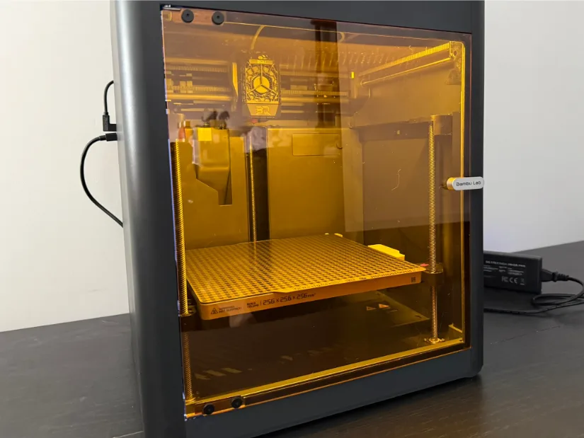 Front view of a Bambu Lab P1S 3D printer fitted with BIGTREETECH’s amber-tinted Panda Door, its empty build plate and tool-head visible through the enclosure on a black workbench.