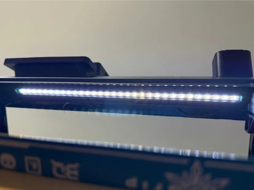 Close-up of the BIGTREETECH Panda LUX LED light bar mounted along the top frame of a Bambu Lab 3D printer, its white LEDs brightly illuminating the build chamber.