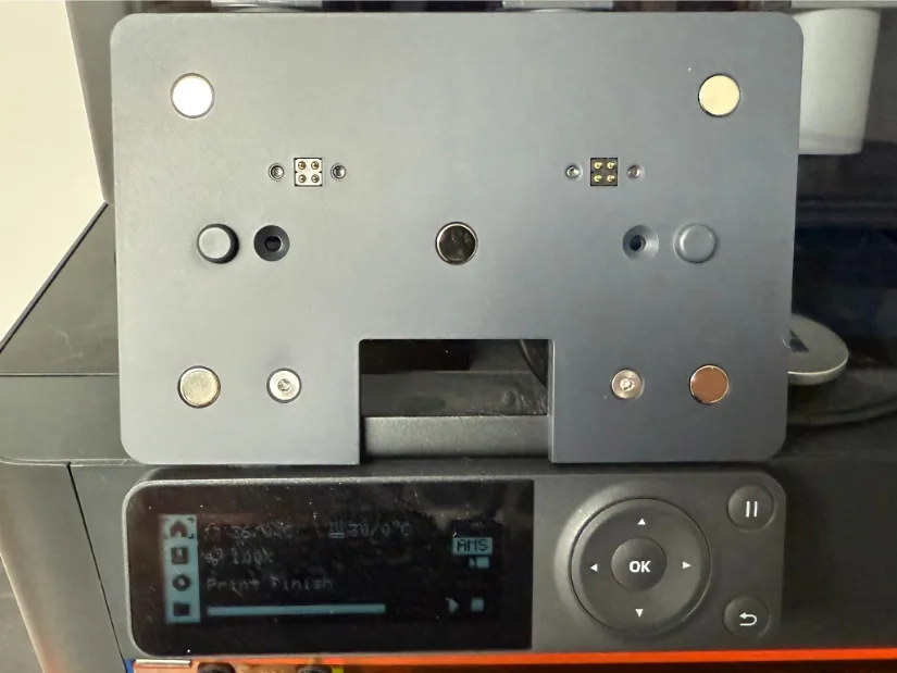 “Rear view of the BIGTREETECH Panda Touch magnetic docking plate mounted above the stock Bambu Lab front control panel, showing pogo-pin connectors, alignment pegs, and neodymium magnets ready to hold the handheld touchscreen.