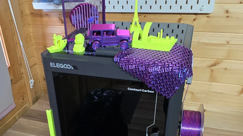 Multiple completed 3D prints displayed on top of the Elegoo Centauri Carbon, including chainmail, test models, a vehicle, and Eiffel Tower