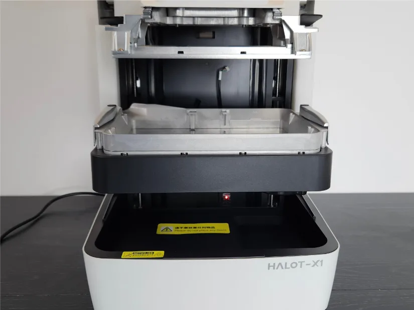 Piocreat HALOT-X1 interior with the moving resin vat at mid height above the light engine, fixed solid-mount platform visible