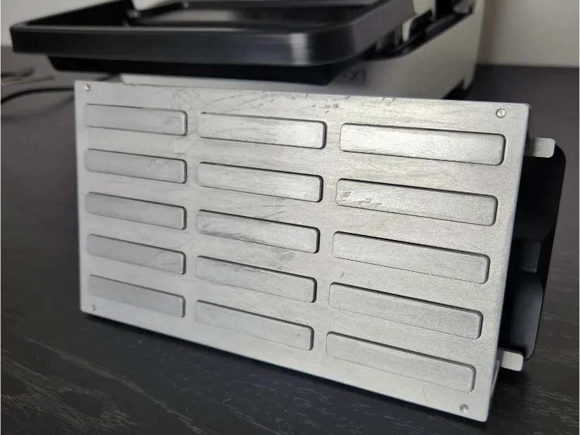 Piocreat HALOT-X1 quick-release build plate underside showing slotted recesses/grip channels on the aluminum surface, with handle assembly at right