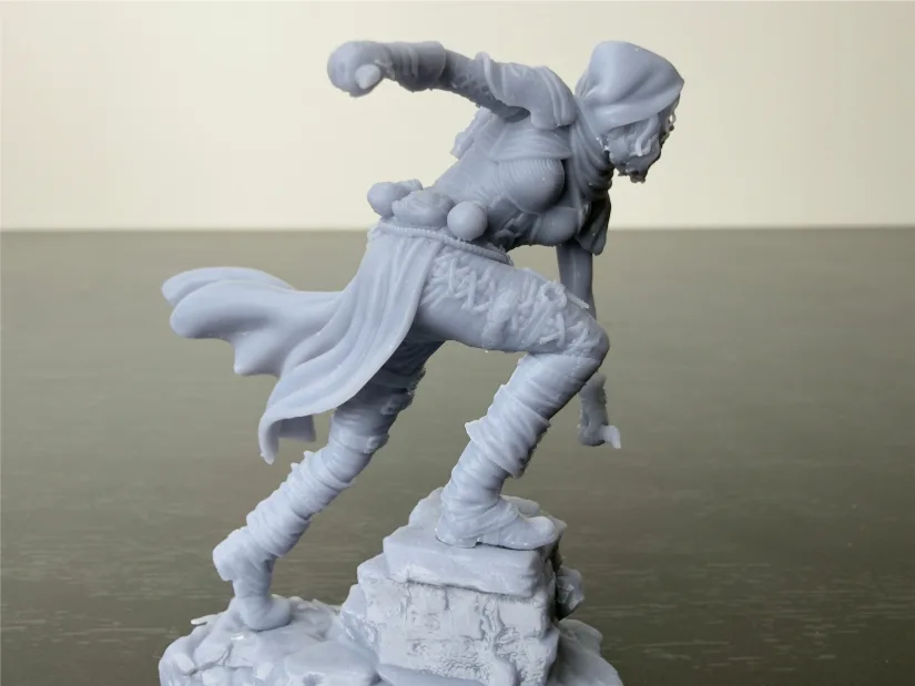 Nerikson Enika the Assassin 75 mm resin miniature side profile—flowing cape, laced leggings—unpainted gray on rock base, printed on Piocreat HALOT-X1