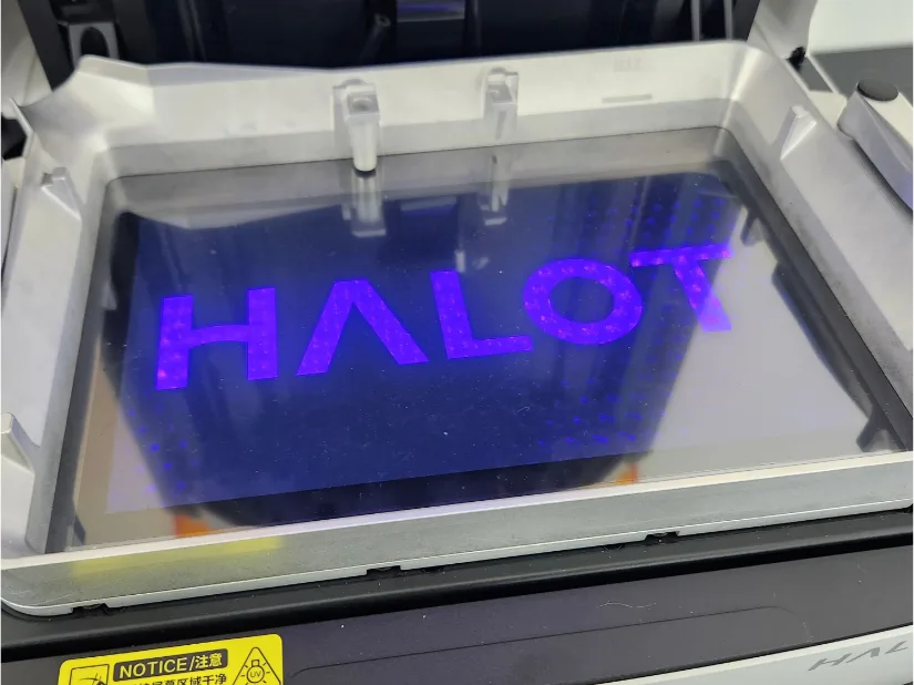 Close-up of Piocreat HALOT-X1 LCD exposure test—“HALOT” logo glowing violet beneath the resin vat, showing the honeycomb UV light matrix and MAX fill line