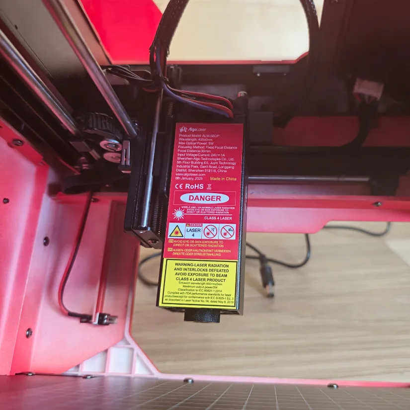 Close-up of the Algolaser Pixi 5W laser module with warning labels and wiring
