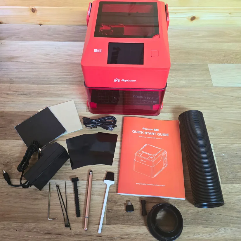 Algolaser Pixi laser engraver with included accessories laid out on a wooden surface