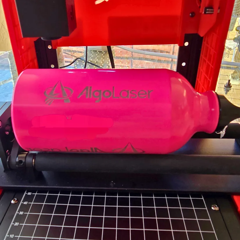 Algolaser Pixi engraving brand logo onto pink coated metal bottle using rotary roller attachment