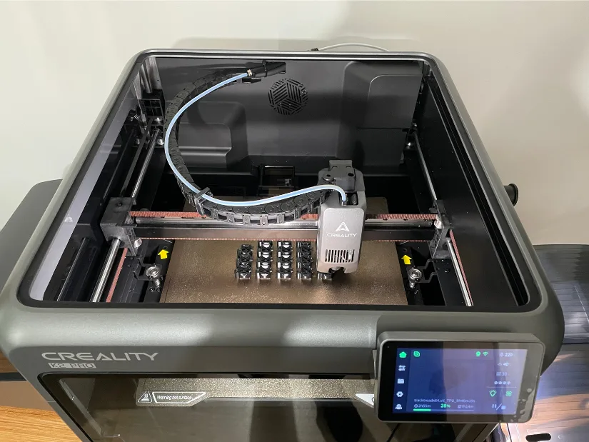 Batch of TPU track treads being 3D printed on the Creality K2 Pro, visible through the open top with the nozzle mid-print.