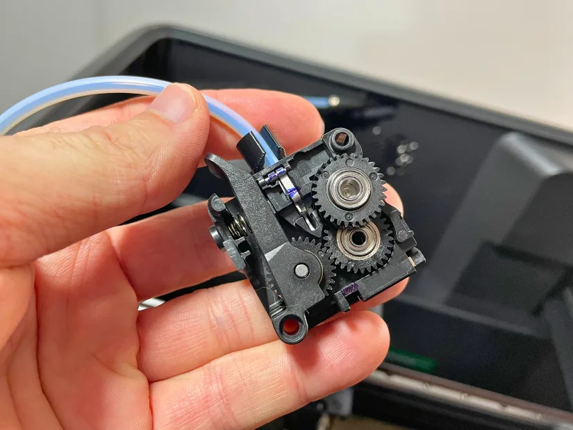 Close-up of the Creality K2 Pro extruder with gears exposed during disassembly for filament jam clearing and blade replacement