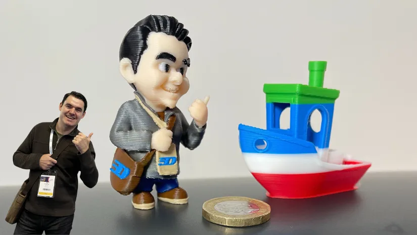 CubeMe character generated from a 2D photo and then 3D printed in 8 colours, shown next to a multicolor Benchy boat