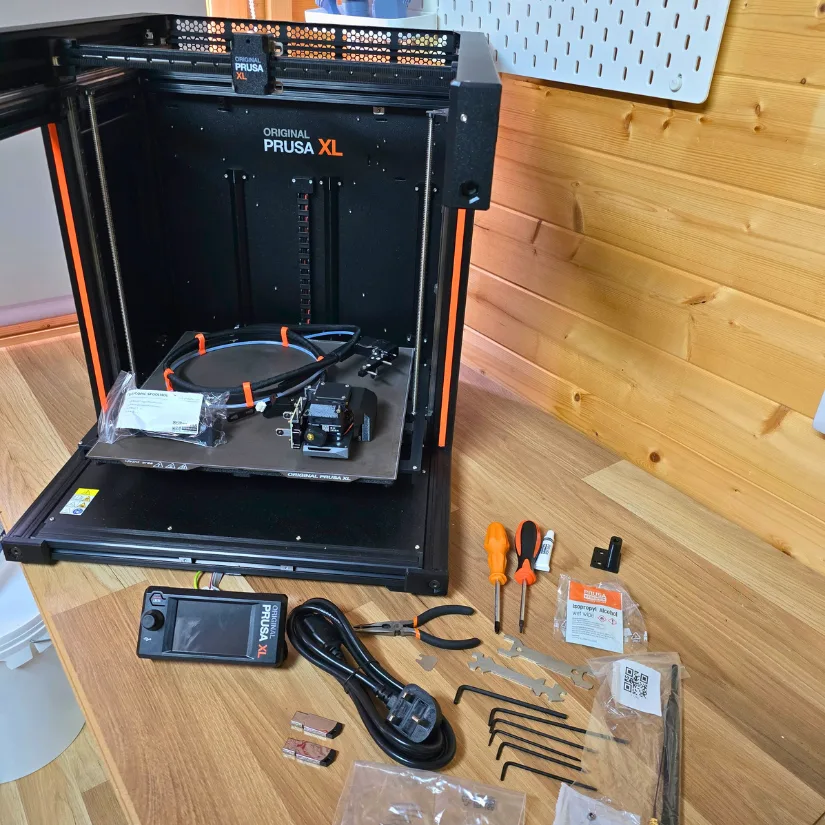 Prusa XL semi-assembled with one tool head, LCD screen, power cable, toolkit, and accessories on wooden desk