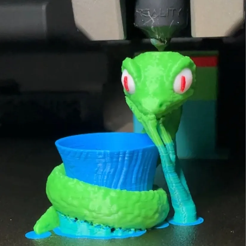 Close-up of a snake model 3D printed in four colors on the Creality K2 Pro, showing green body, blue base, white eyes, and red pupils.