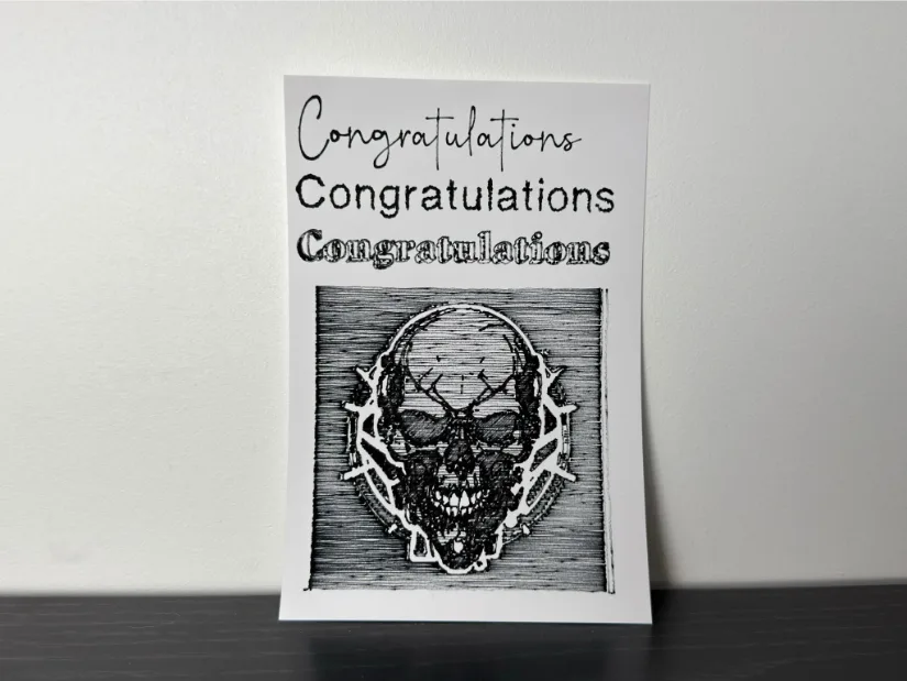 Pen-plotted sample on white cardstock showing three “Congratulations” headings in different fonts and a cross-hatched skull illustration below.