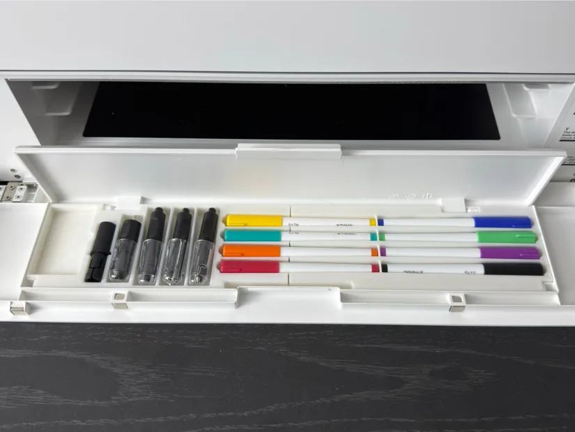 Riser Base front storage compartment of the xTool M1 Ultra, showing organized slots holding tool heads/adapters and a row of colored pens.