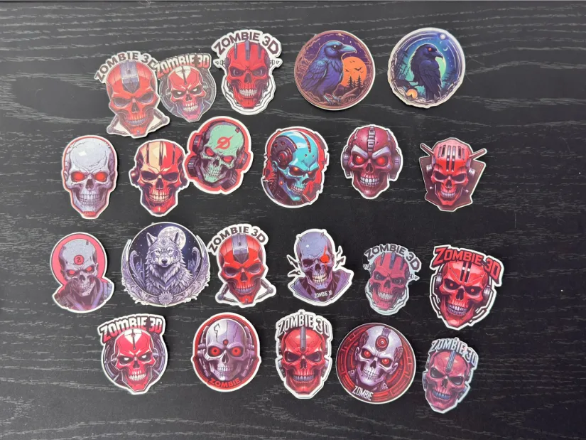 Assorted holographic and glossy stickers made with the xTool M1 Ultra, featuring zombie/skull designs and two raven illustrations, neatly arranged on a black tabletop