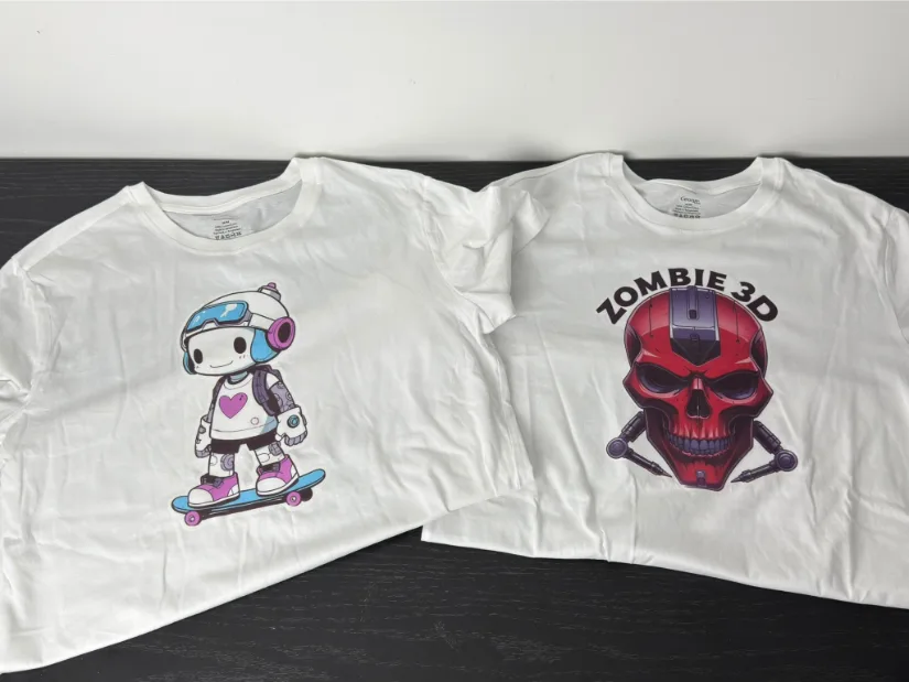 Two white T-shirts with inkjet iron-on transfers applied: left shirt shows a cute robot on a skateboard; right shirt features a red “ZOMBIE 3D” skull graphic.