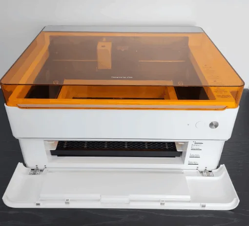 xTool M1 Ultra desktop machine with amber safety lid and front access door open, showing the honeycomb bed and interior carriage.