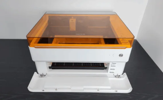 xTool M1 Ultra desktop machine with amber safety lid and front access door open, showing the honeycomb bed and interior carriage.
