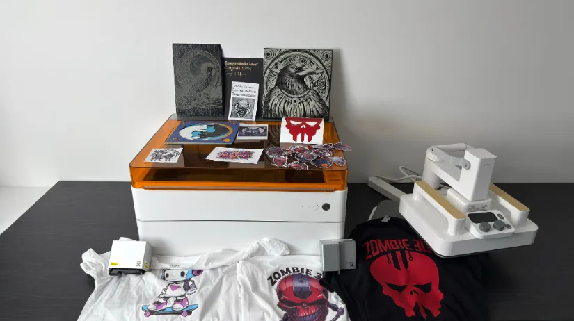 Group shot of the xTool M1 Ultra with finished projects—slate and canvas engravings, stickers, foil card, vinyl decal, multi-layer papercut, and two T-shirts—plus the Smart Heat Press at right.