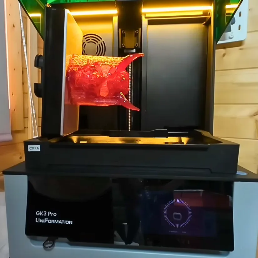 Uniformation GK3 Pro build plate resting on the side drain holder with a red resin print attached