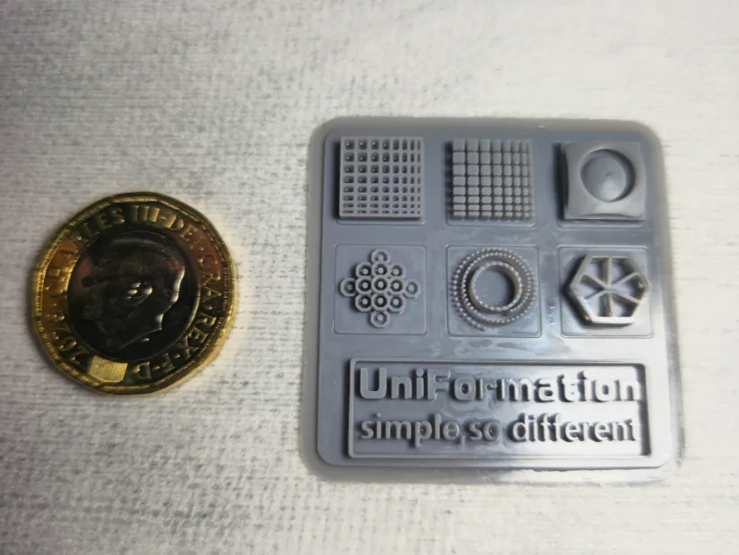 Uniformation GK3 Pro resin test print card next to a coin showing fine detail and resolution