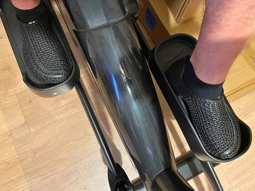 PollyFab Flux black 3D printed lattice shoes being tested on a Reebok cross trainer, showing foot placement and comfort during exercise.