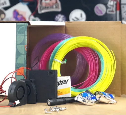 Print kit contents including colorful 3D printing filament, electronics, fan, battery, and hardware components laid out on a workbench