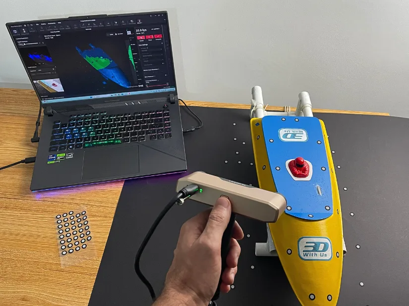 Using the Revopoint Inspire 2 3D scanner to capture the top of a yellow RC boat, with Revo Metro software running on a laptop in the background