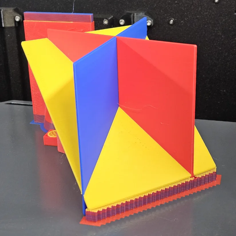3D printed model of three intersecting planes on a build plate with visible support structures and color transitions