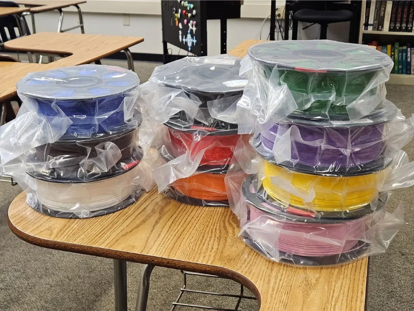 Spools of 3D printing filament stacked on classroom desks, donated to support the creation of educational math models