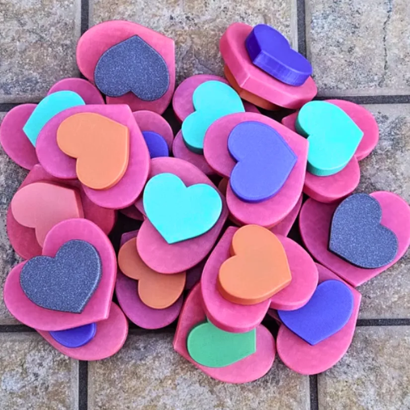 A batch of 3D printed triple heart fidget spinners in multiple colors prepared for classroom Valentine exchanges