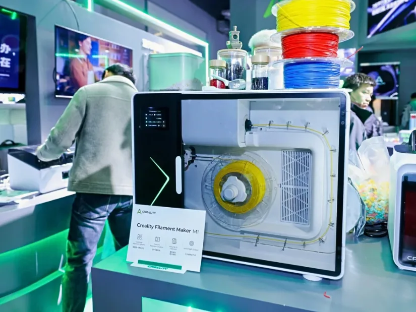 Creality Filament Maker M1 displayed at a trade show with sample filament spools and recycled material