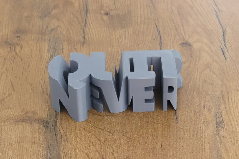 Finished NEVER QUIT text-flip 3D print on a wooden surface